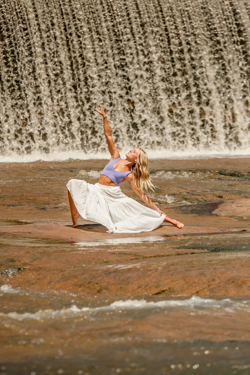 A photo showing a dancer posing in front of a waterfall in a white dress.