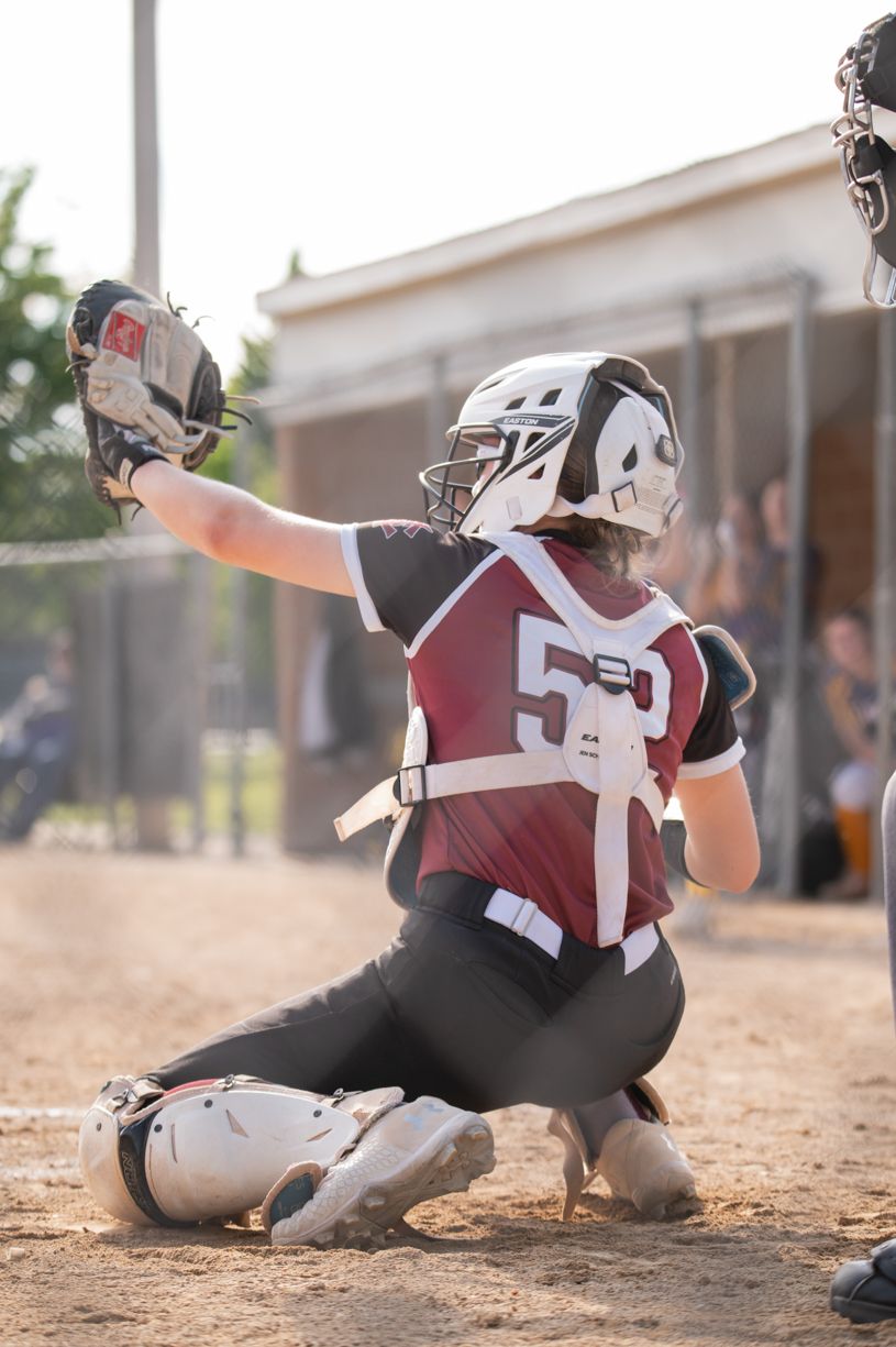 Catcher in maroon and white uniform making a play at home plate.