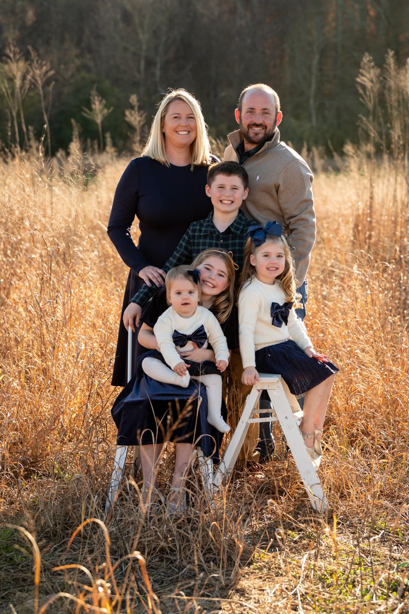 Family sitting together in tall golden grass during an outdoor photo session.