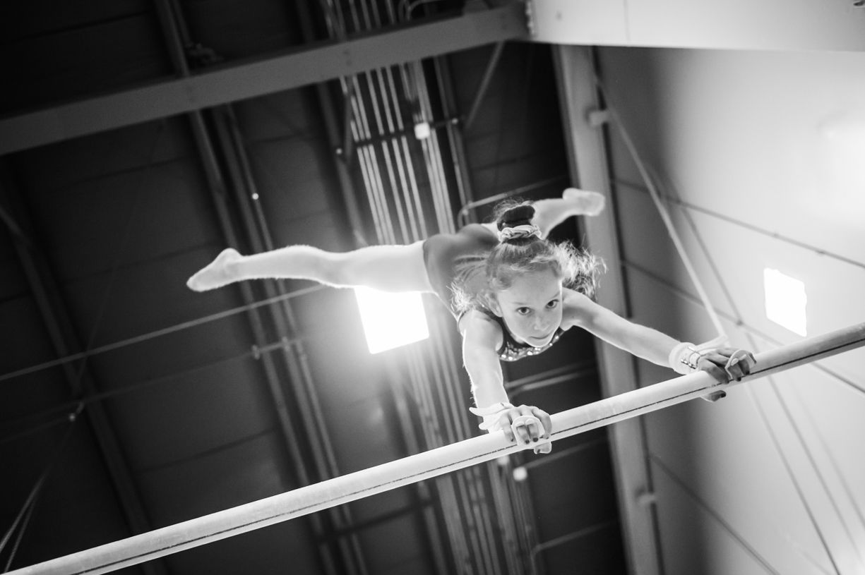 A black and white photos showing gymnast performing on uneven bars.