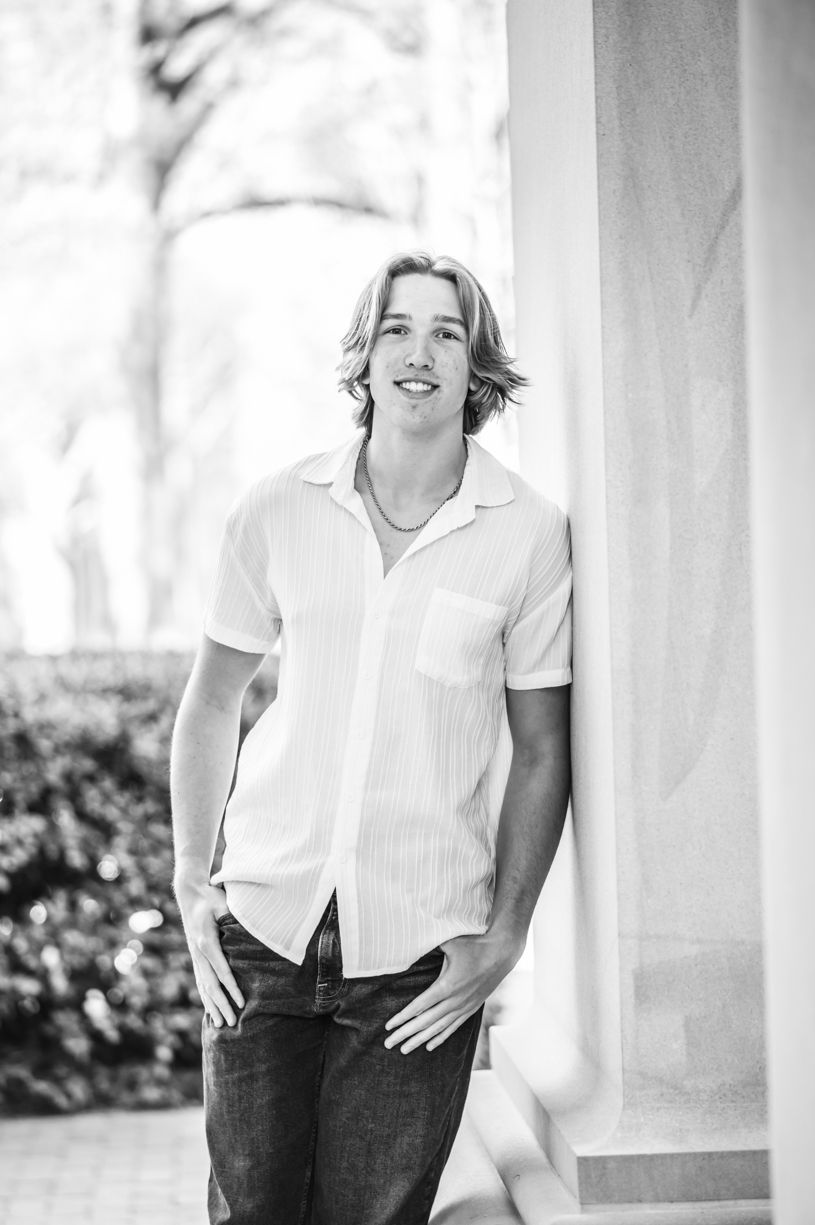 Classic black and white portrait of a senior guy against white columns with soft natural lighting.