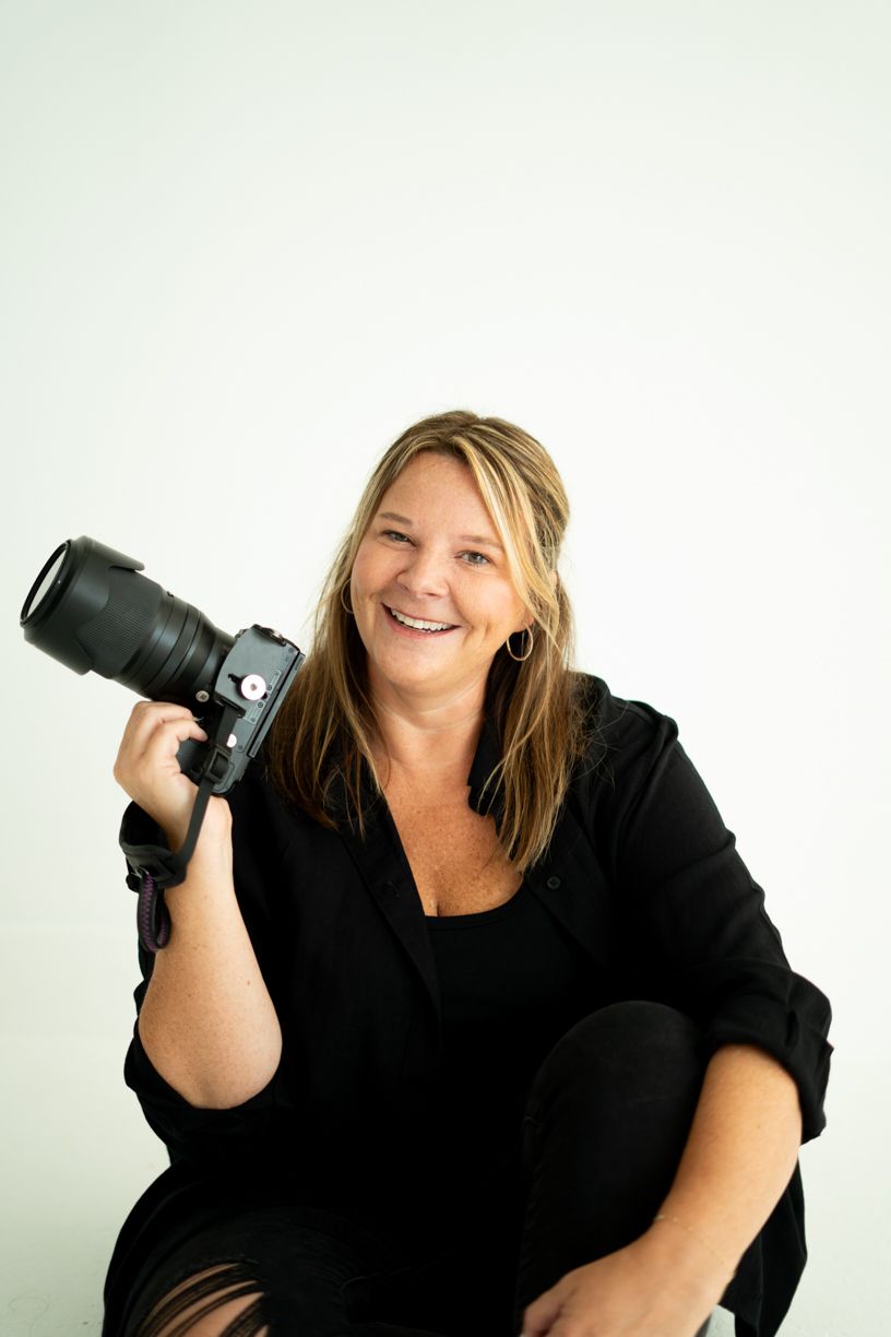 Professional photographer wearing black holding a DSLR camera with telephoto lens against white background.