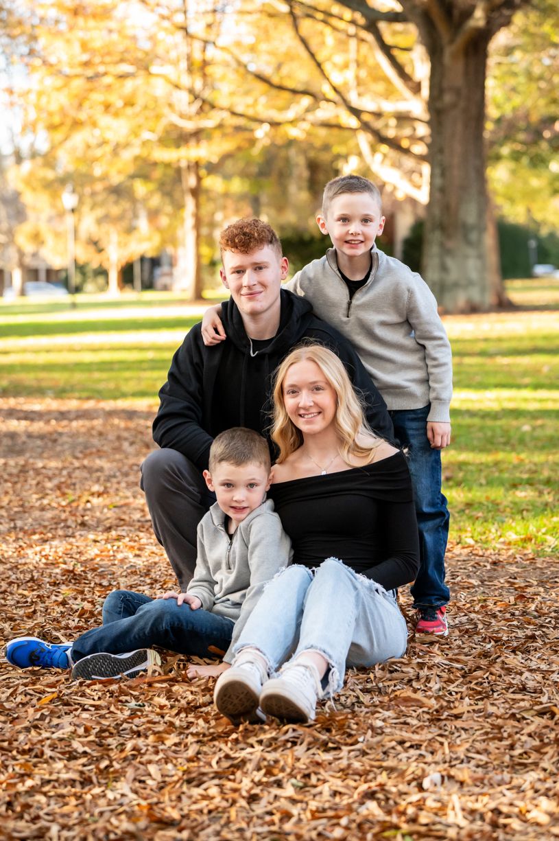 Family group sitting together on autumn leaves under golden trees.