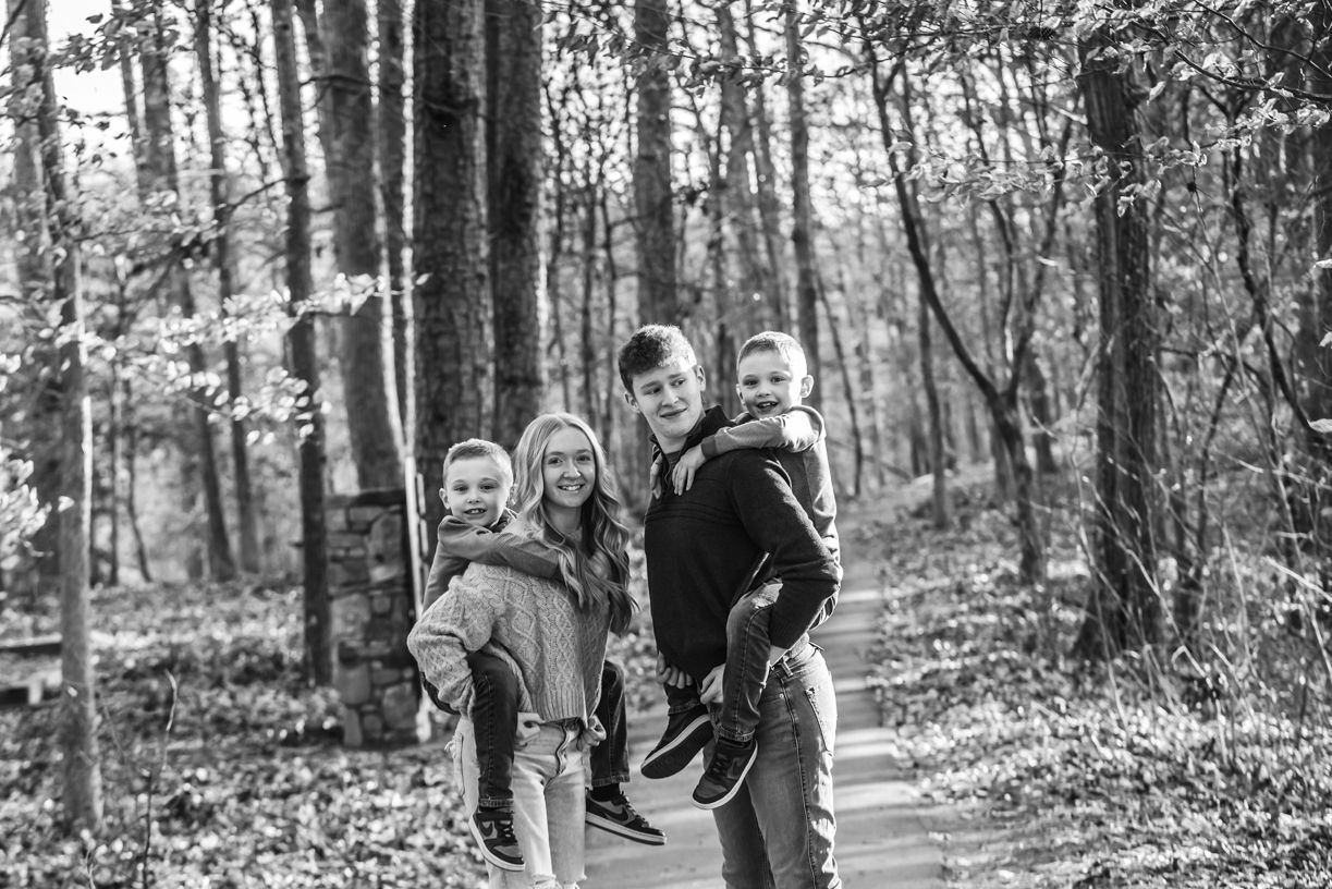 A family enjoying a playful moment together in a wooded setting during autumn.