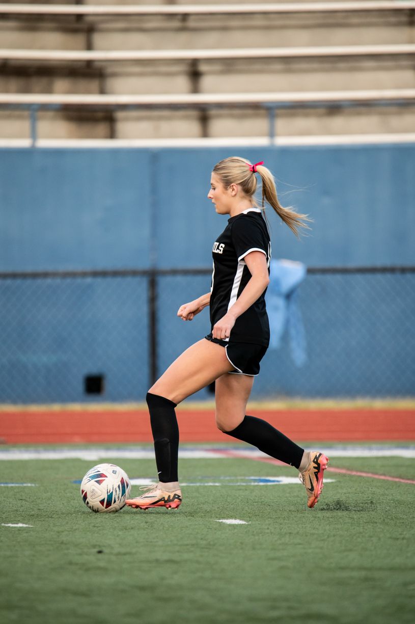Soccer player in black uniform practices ball control drills on turf field.
