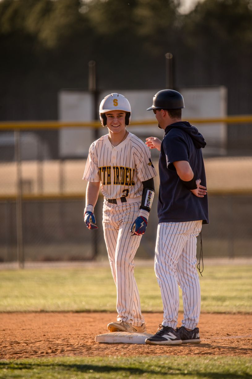Baseball players interact near second base during a game on a sunny field.