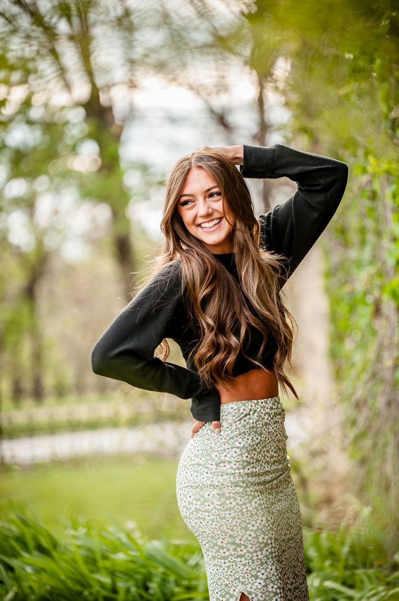 Portrait of senior girl in black crop top and patterned skirt posing in nature setting.