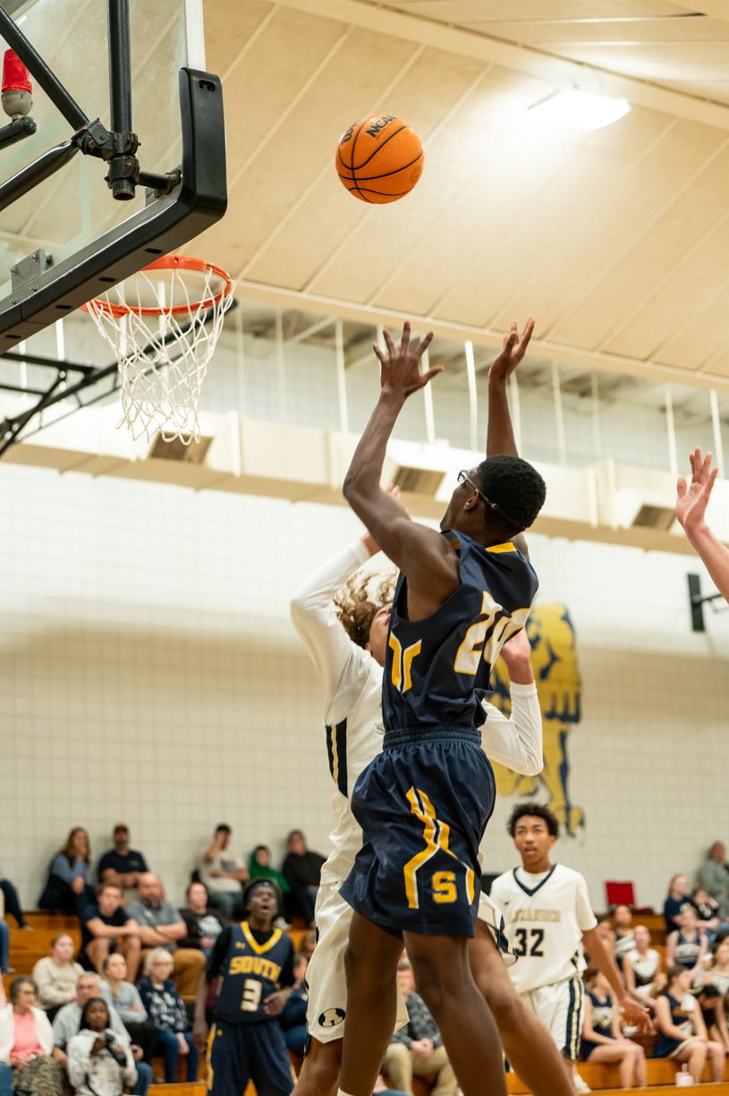 Basketball players jumping for a shot during an indoor game.