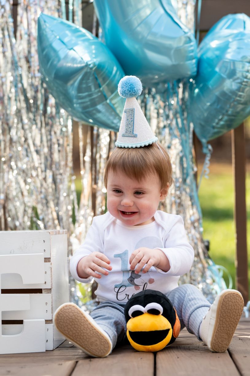 Baby's first birthday celebration with blue balloons and silver tinsel decorations.