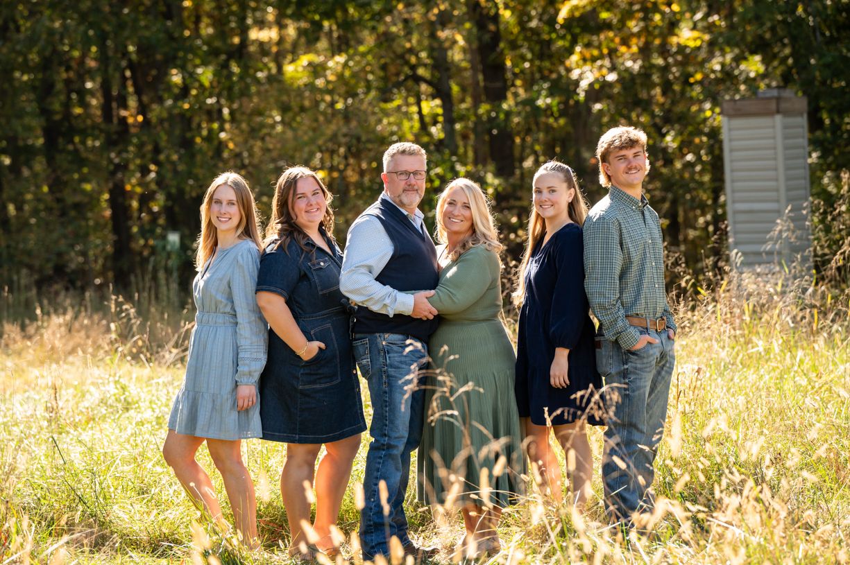 A family poses together in a sun-drenched field with trees in the background.