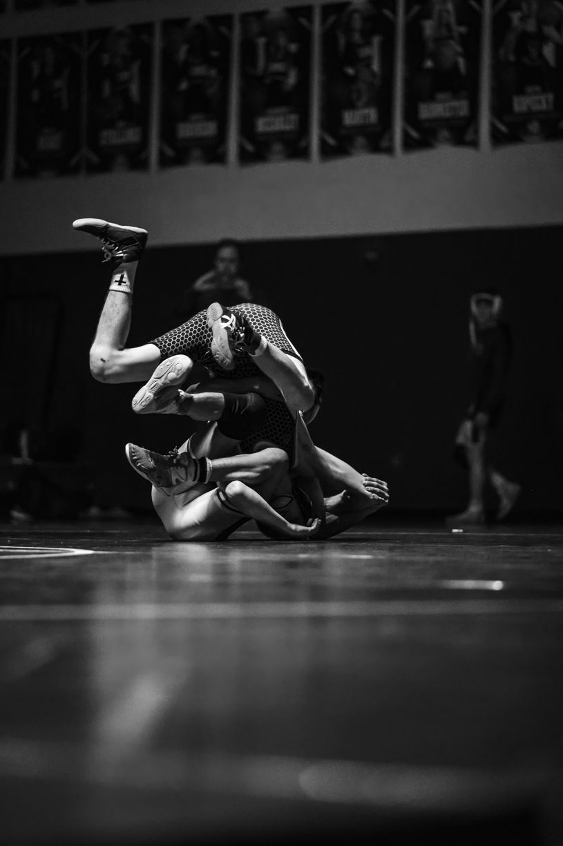 Dramatic black and white shot of wrestlers competing on a mat.