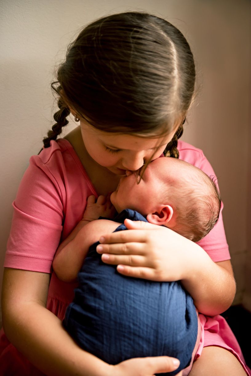 Mother in pink shirt tenderly holding and kissing newborn baby in blue outfit.