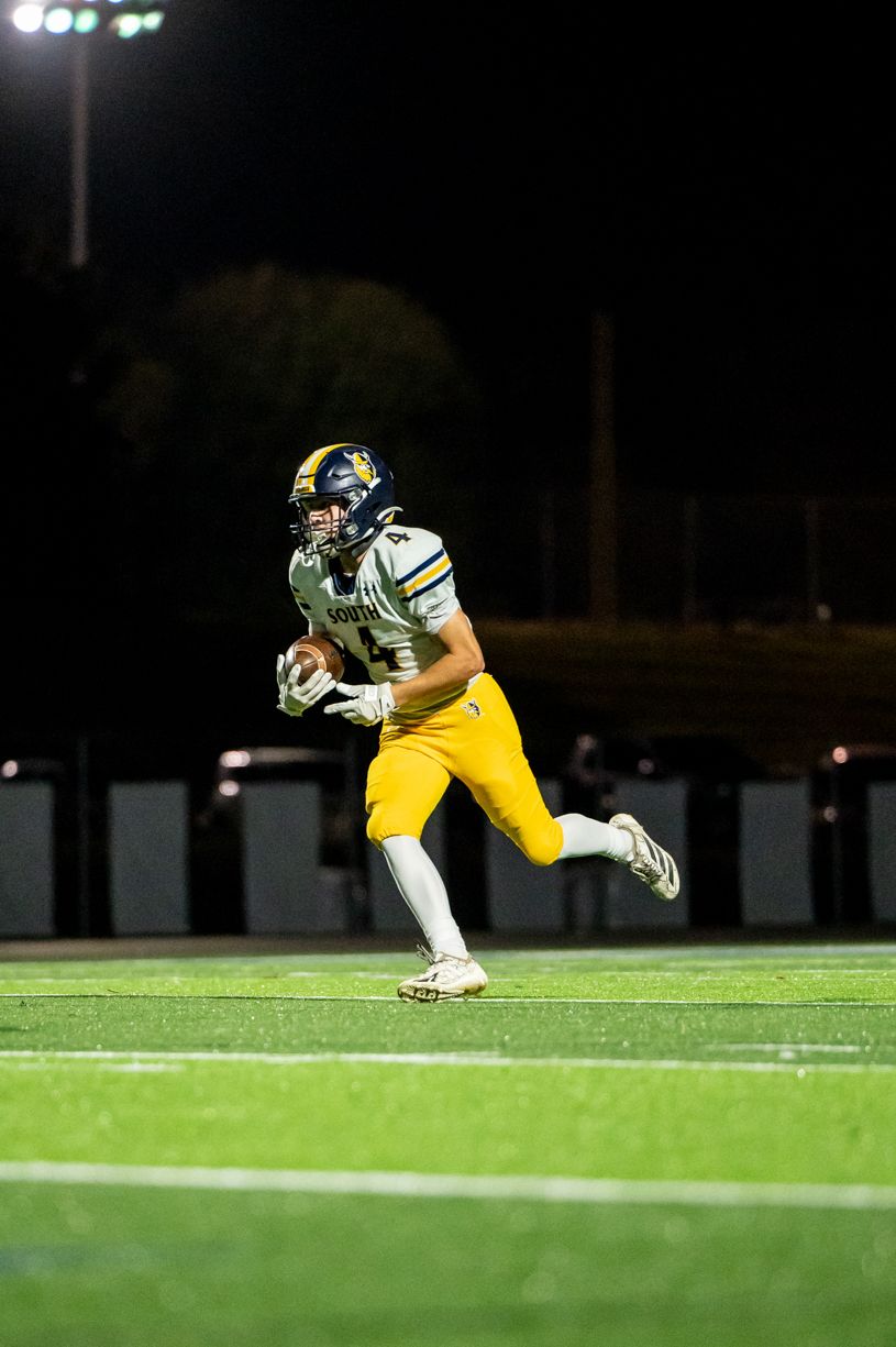 Football player in yellow uniform runs with ball during nighttime game under stadium lights.