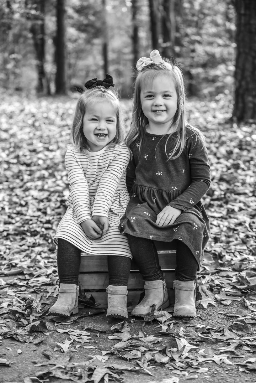 Two children in boots sitting together on fallen autumn leaves.