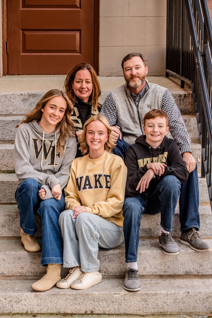 A group sits together on stone steps wearing casual collegiate sweatshirts and jeans.