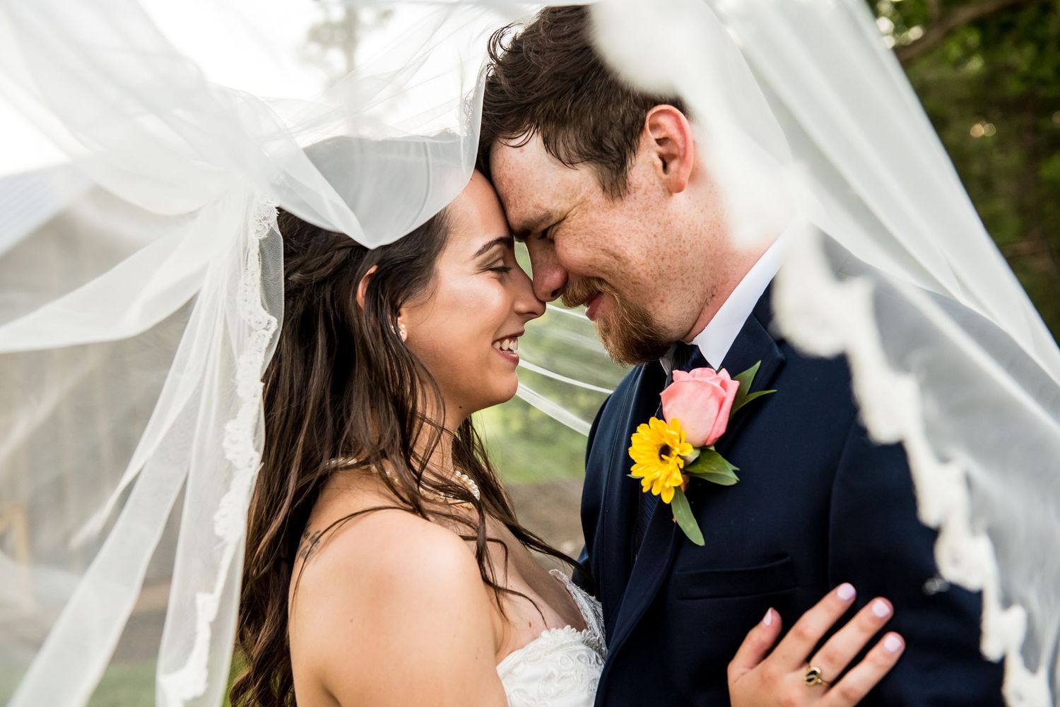 Bride and groom share romantic forehead touch under flowing white veil on their wedding day.
