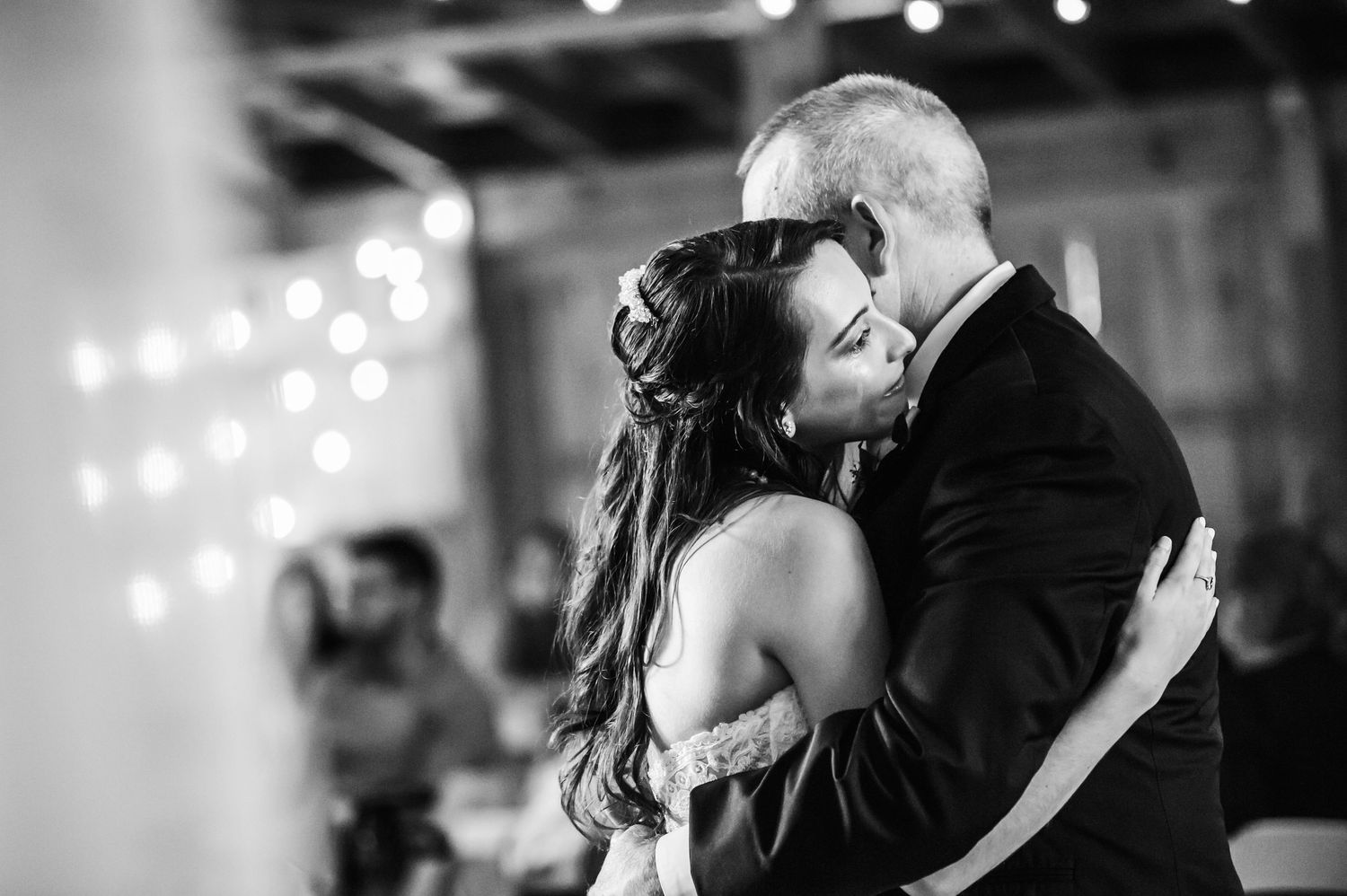 Black and white photo of a couple sharing a romantic first dance embrace at a wedding reception.
