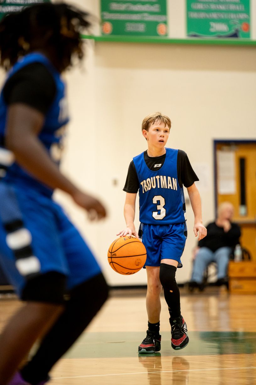 Young basketball player in blue jersey dribbling on indoor court during practice.