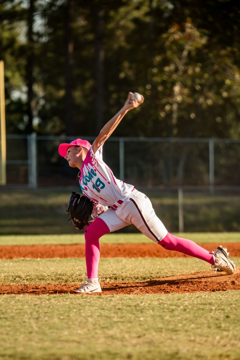 Baseball player in pink uniform sliding dramatically on dirt field during game.