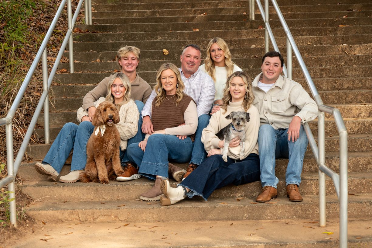 Family portrait on wooden steps with pet dog in casual attire.