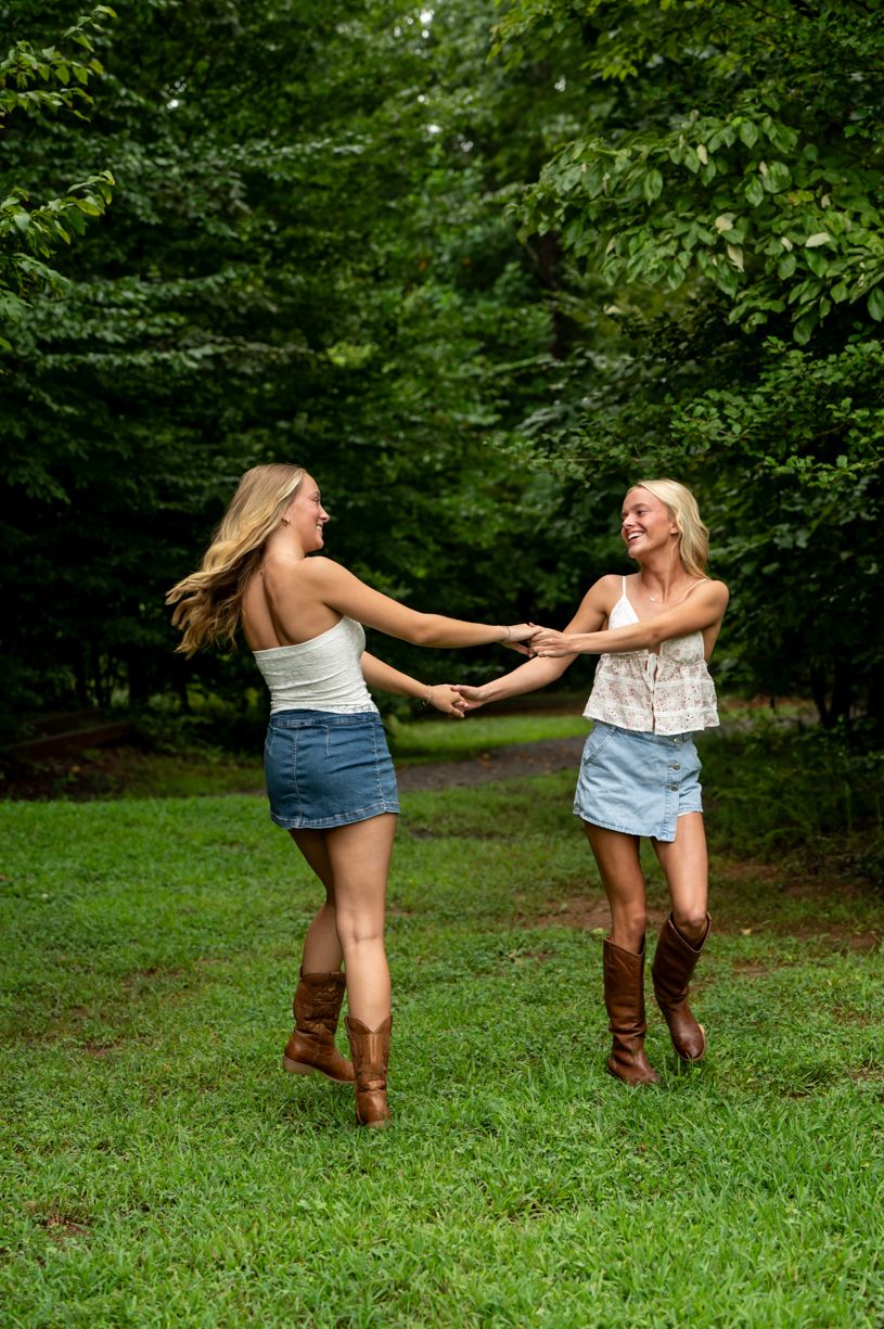 Two friends in casual summer outfits dance and spin in a green park setting.