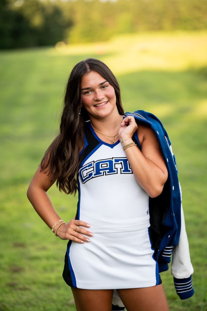 A senior cheerleader featuring a blue and white uniform against a sunny outdoor background.