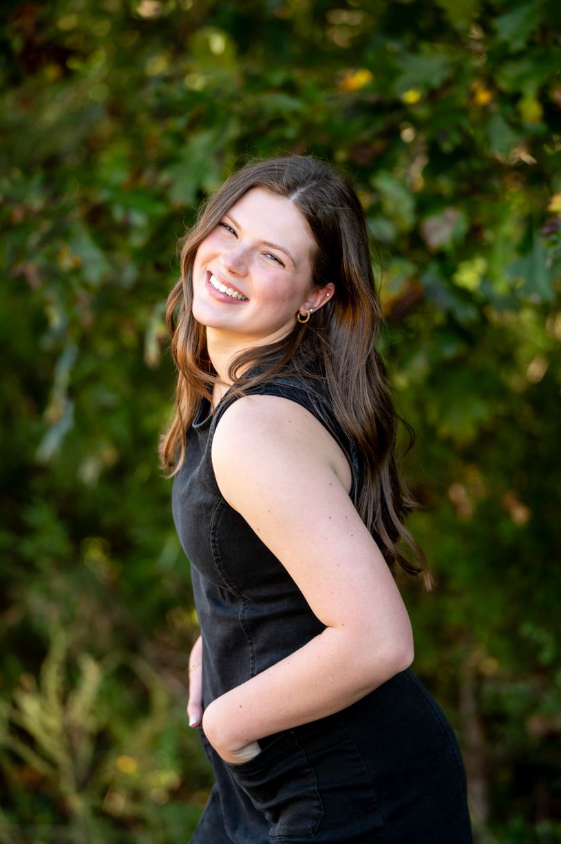 A senior girl wearing in black top against green foliage background during sunset.
