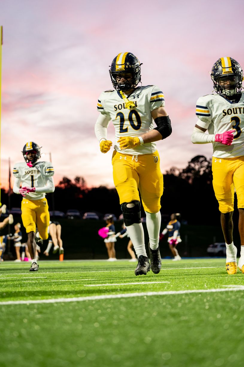 Football players in yellow jerseys running during sunset game.