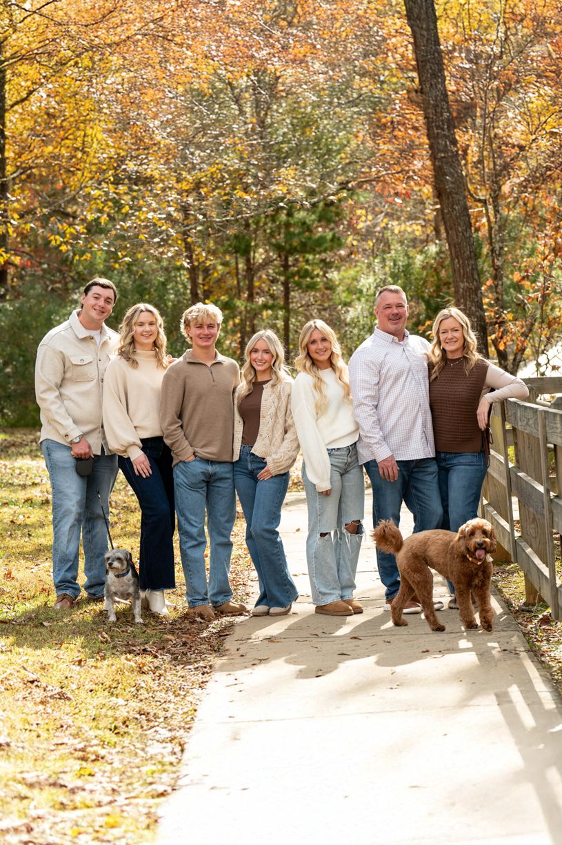 Family group photo with dog against wooden fence in autumn setting.
