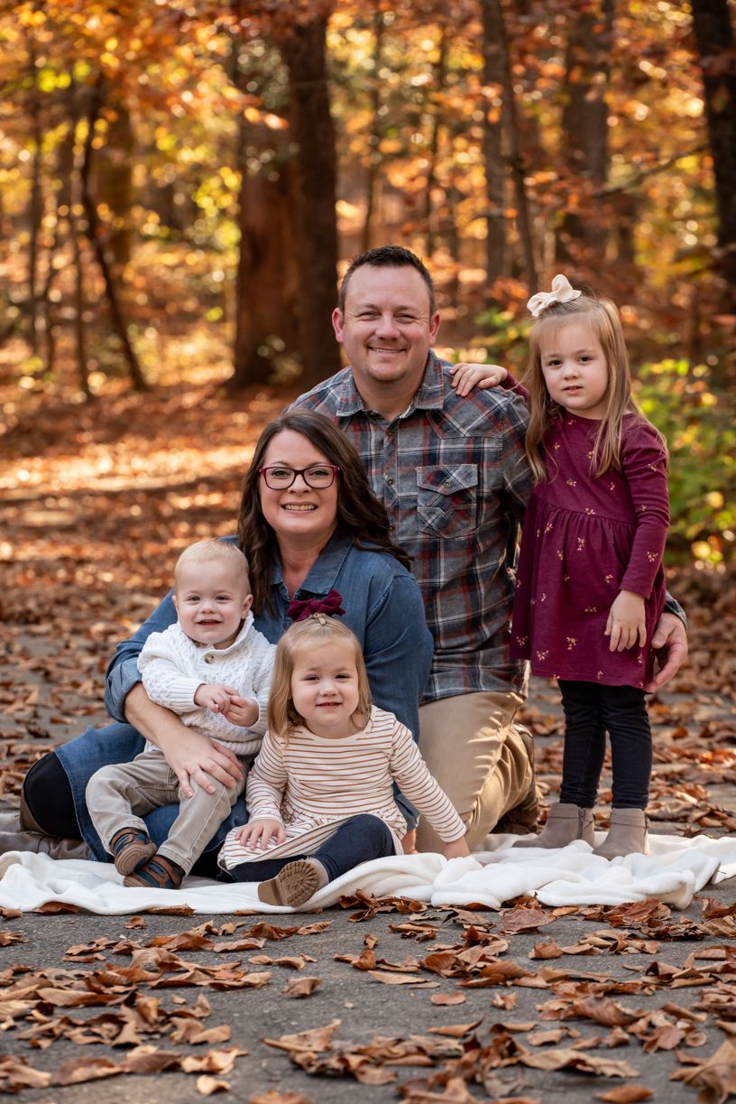 Family autumn portrait session with fall leaves on ground.