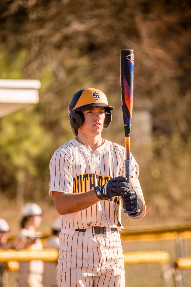 Baseball player in pinstripe uniform takes batting practice during golden hour.