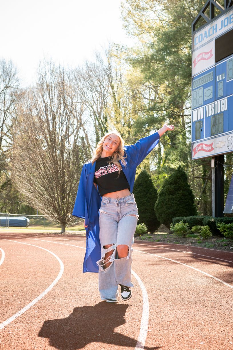 A graduate poses on a red track with blue athletic equipment in the background.