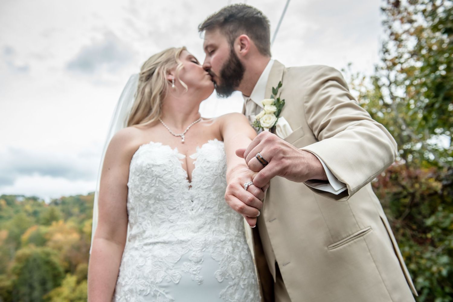 Bride and groom sharing a kiss outdoors on their wedding day, with autumn foliage in the background.