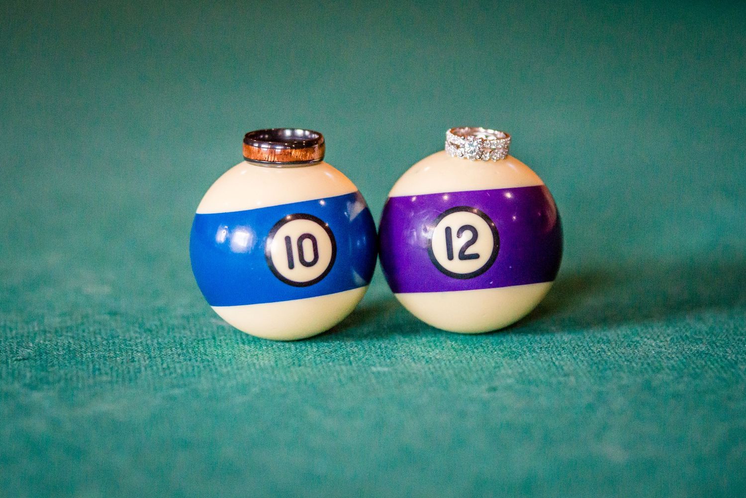 Wedding rings displayed on billiard balls numbered 10 and 12 on a green pool table felt surface.