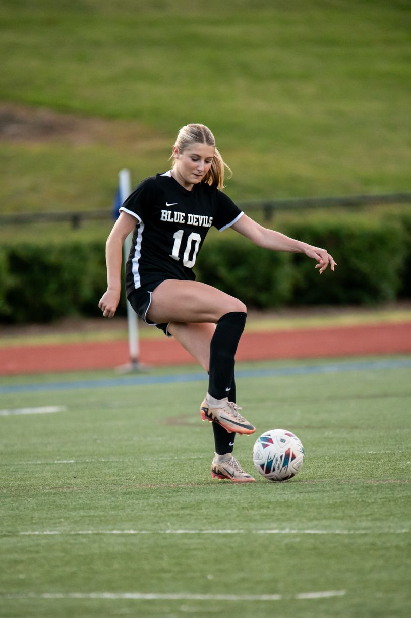Soccer player in black uniform executes sliding kick on athletic field.