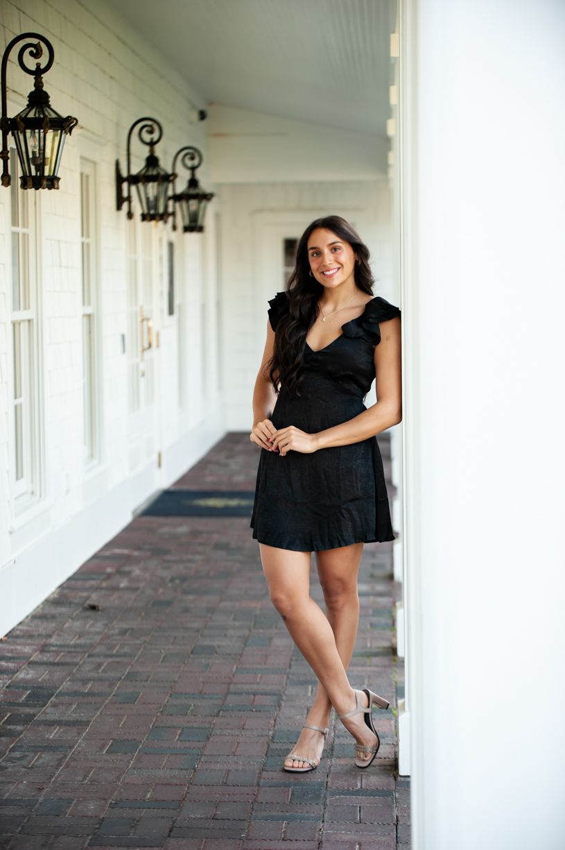 Senior girl posing along a white columned walkway wearing a black dress.