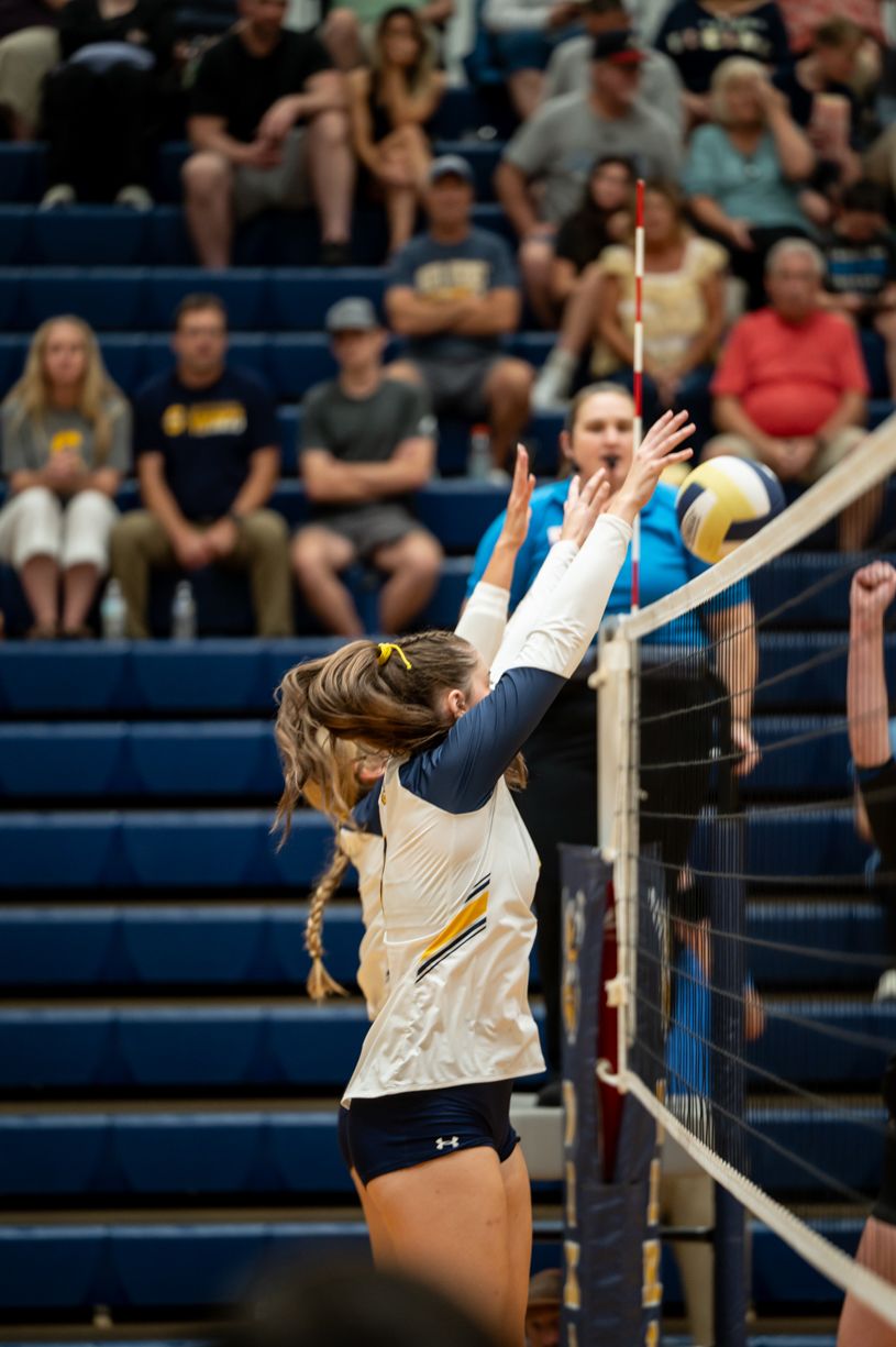 Volleyball players jump at the net during an intense match in a gymnasium.