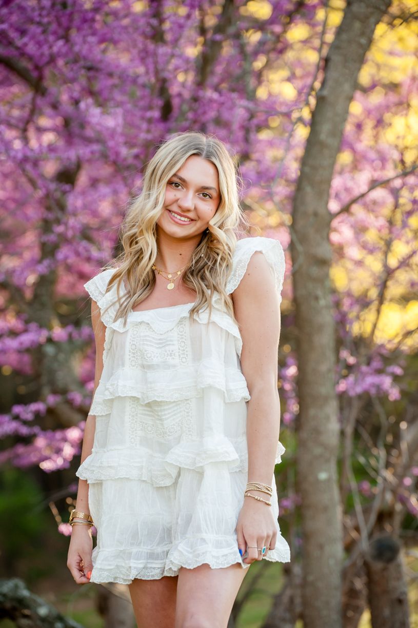 Spring portrait session of a senior girl among blooming purple cherry blossom trees at sunset.