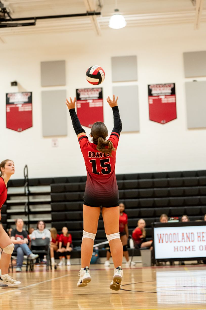 Volleyball player in red jersey setting ball during indoor match.