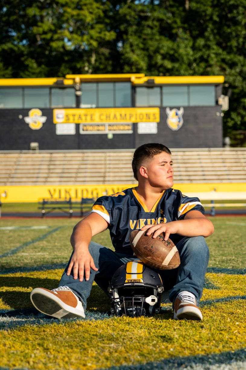 Athletic player resting on football field with stadium bleachers visible.