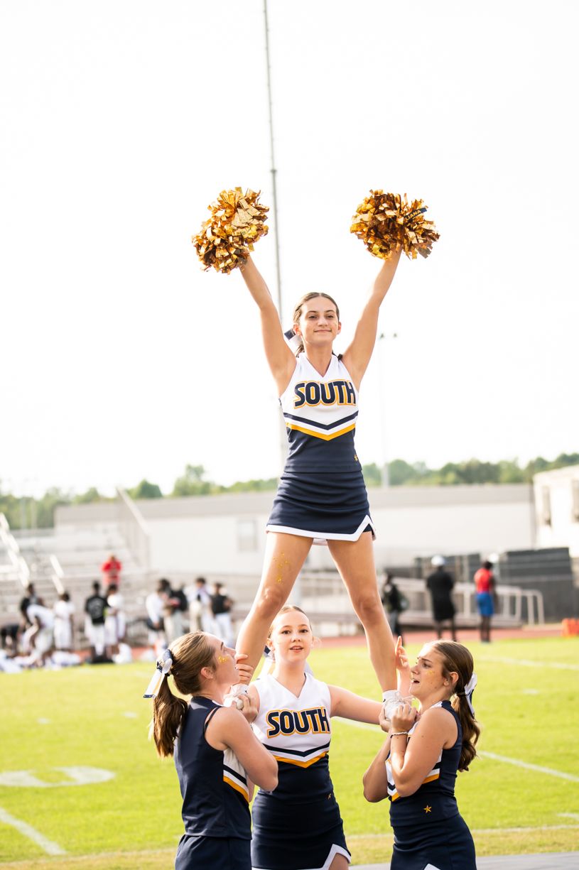 Cheerleaders in navy uniforms performing stunts on football field.