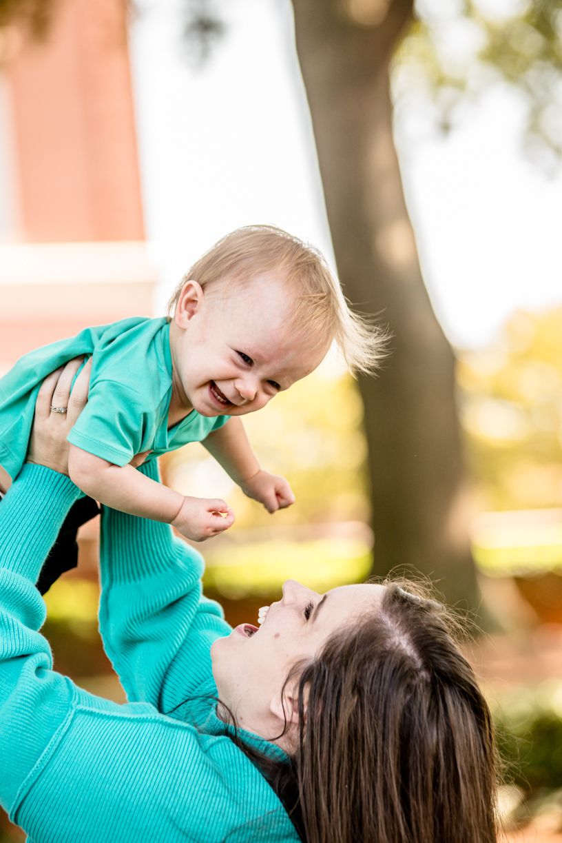 A joyful moment captured between parent and baby playing outdoors in bright sunlight.