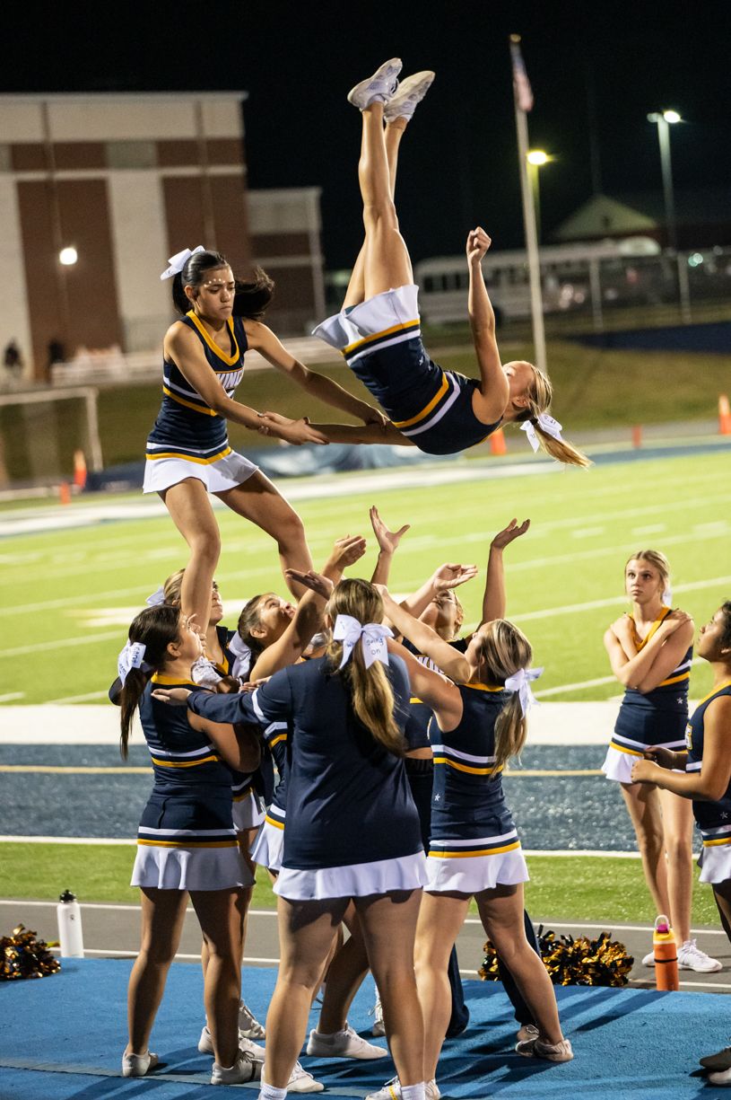 Cheerleaders performing stunts and lifts during a nighttime football game.