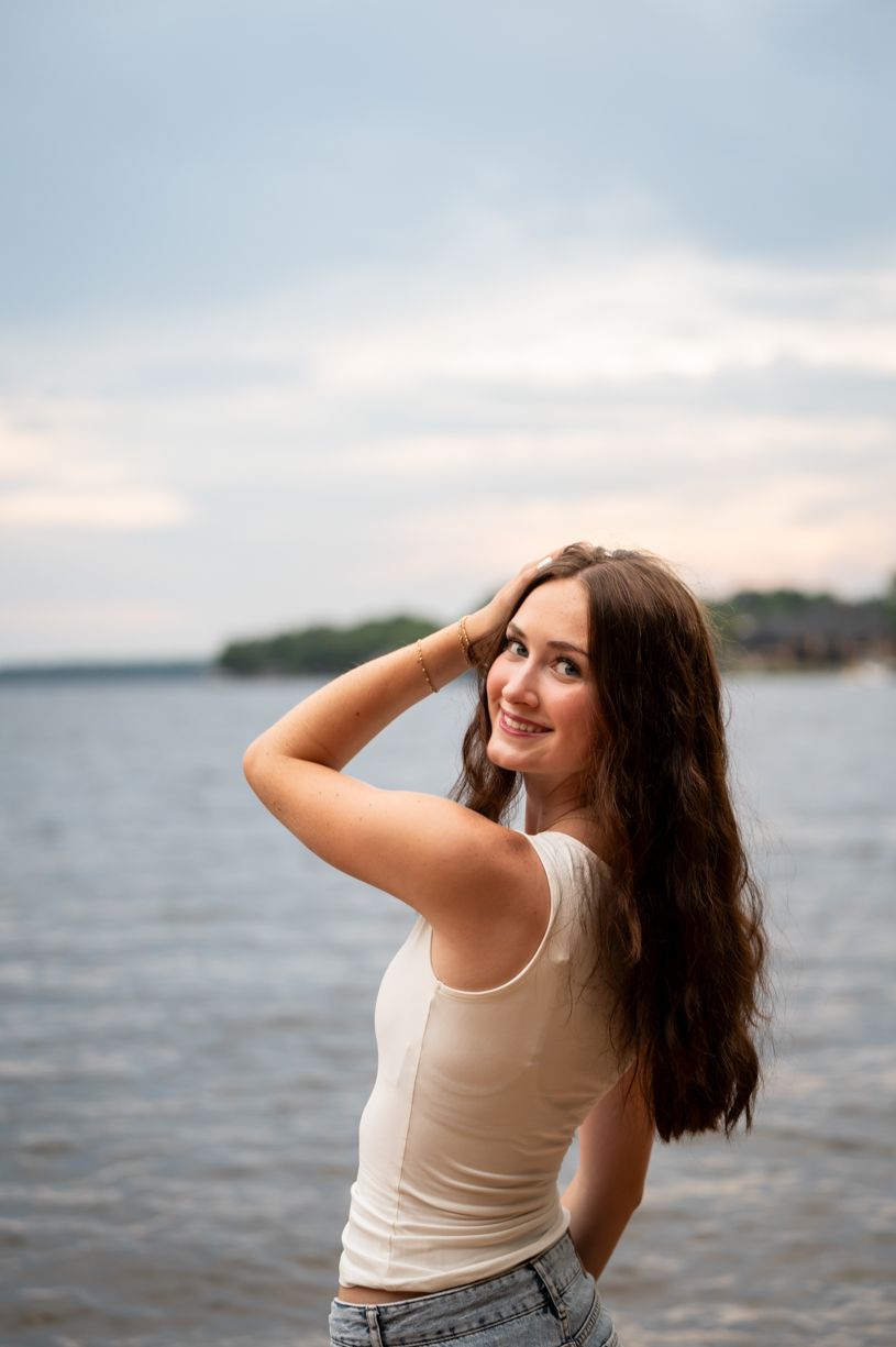 Waterfront portrait at sunset of a senior girl wearing casual attire against lake backdrop.