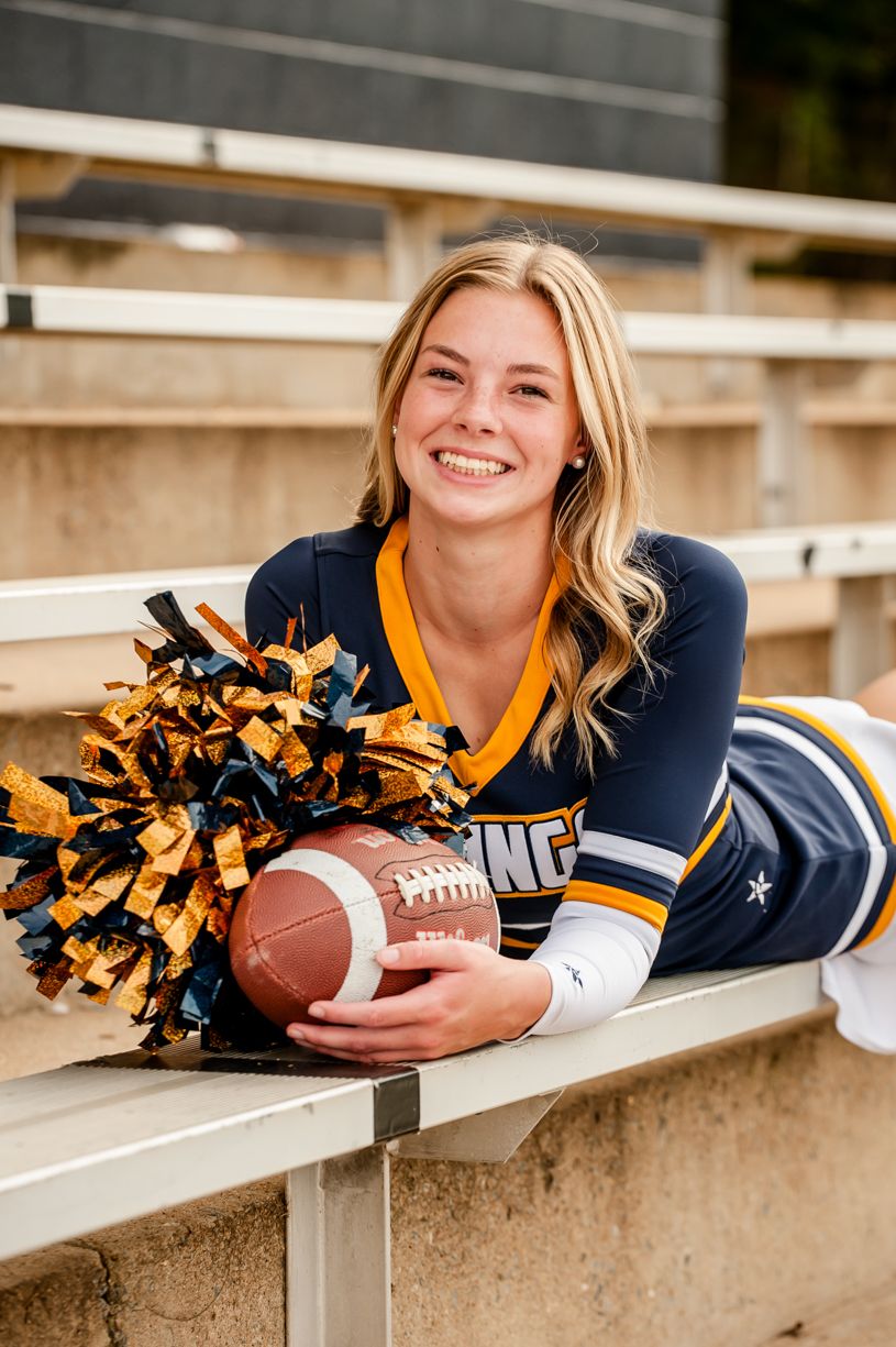 Cheerleader with pom poms and football lying on concrete bleachers in school colors.