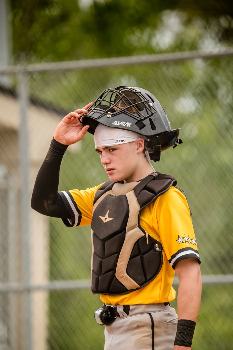 Baseball catcher in yellow uniform and protective gear looking up during a game.