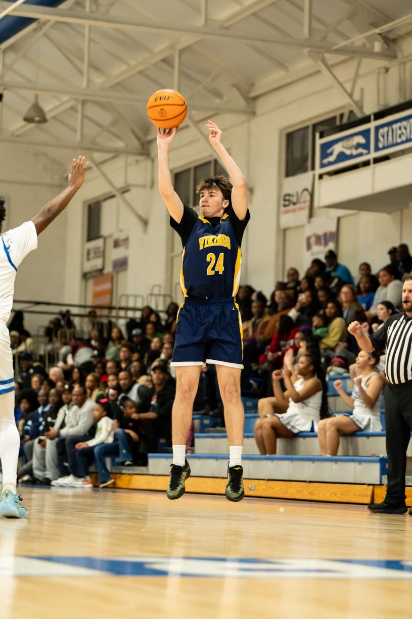 Basketball player in navy jersey number 24 takes a jump shot during a game in a gymnasium.