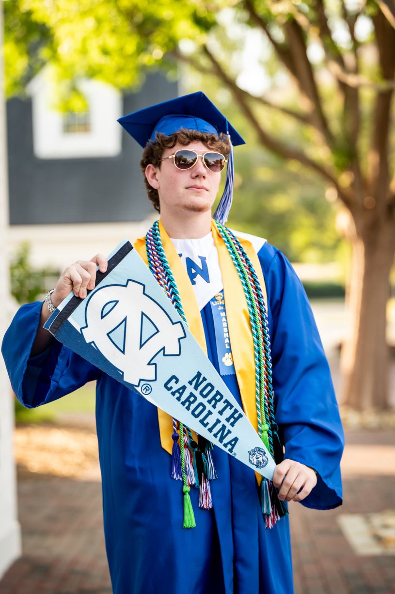 A graduate in blue regalia displaying a UNC sash and decorative cords.