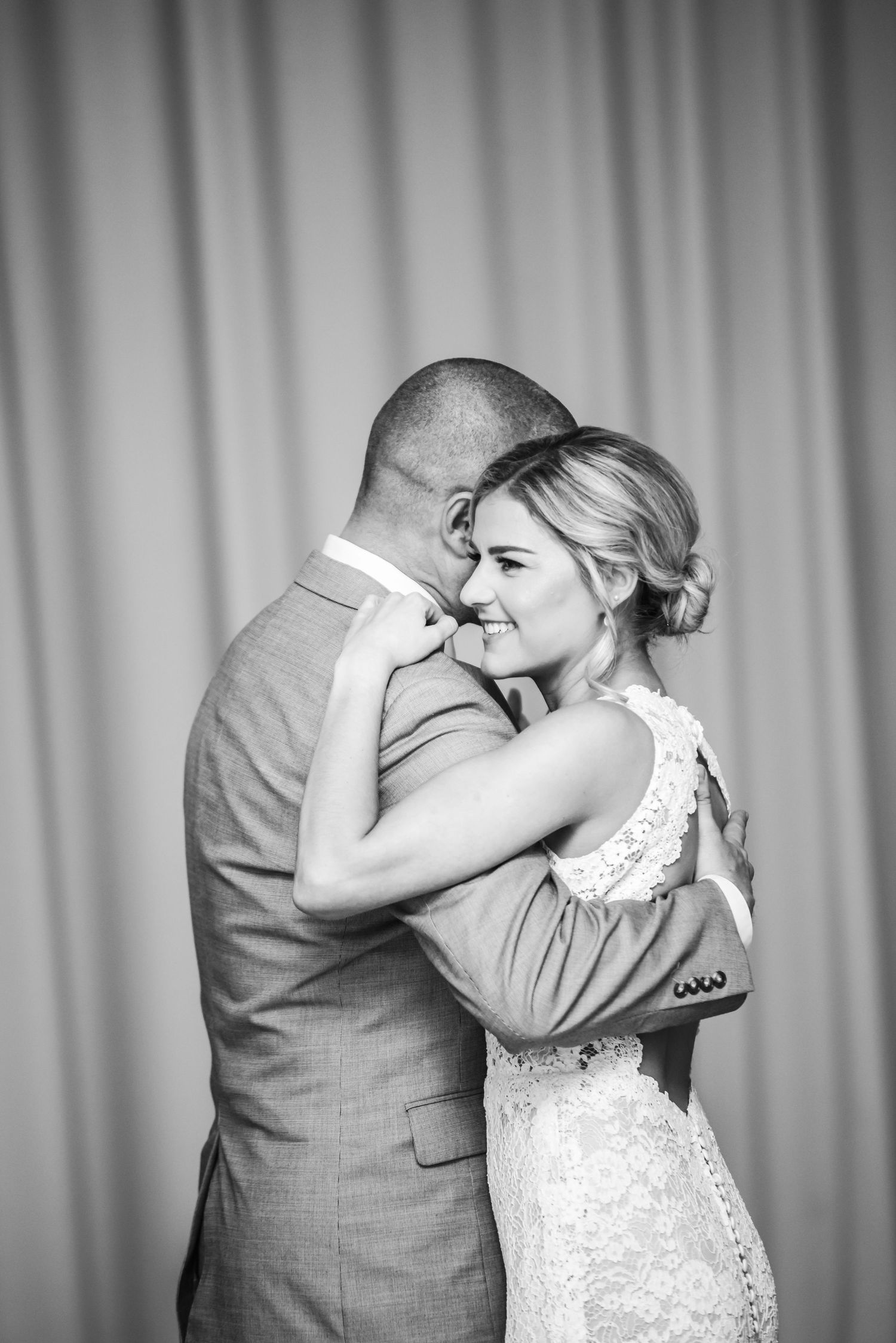 Black and white photo of a bride and groom sharing their first dance, embracing tenderly at a wedding reception.