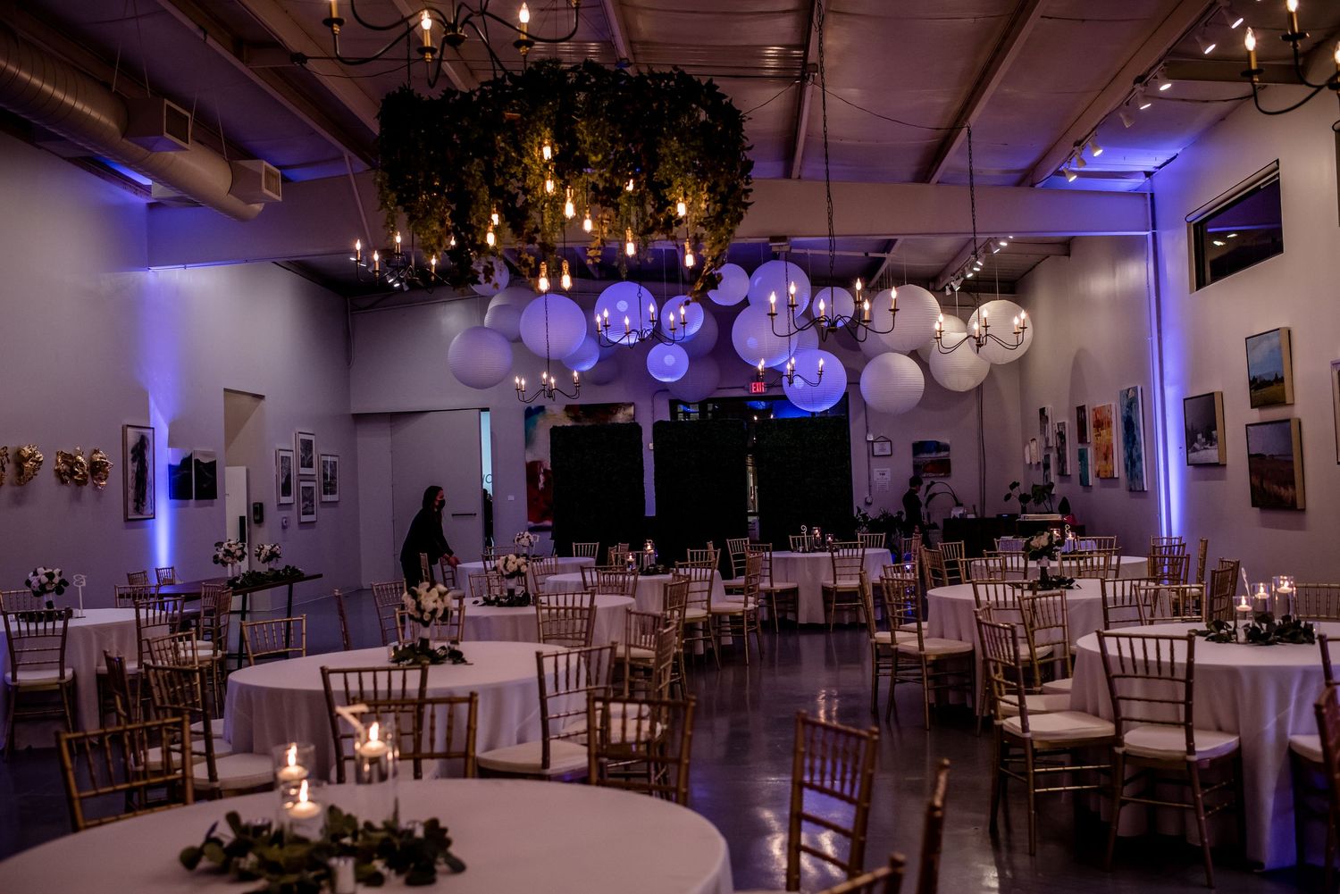 Elegant wedding reception hall with globe pendant lights, chiavari chairs, round tables, and purple uplighting.